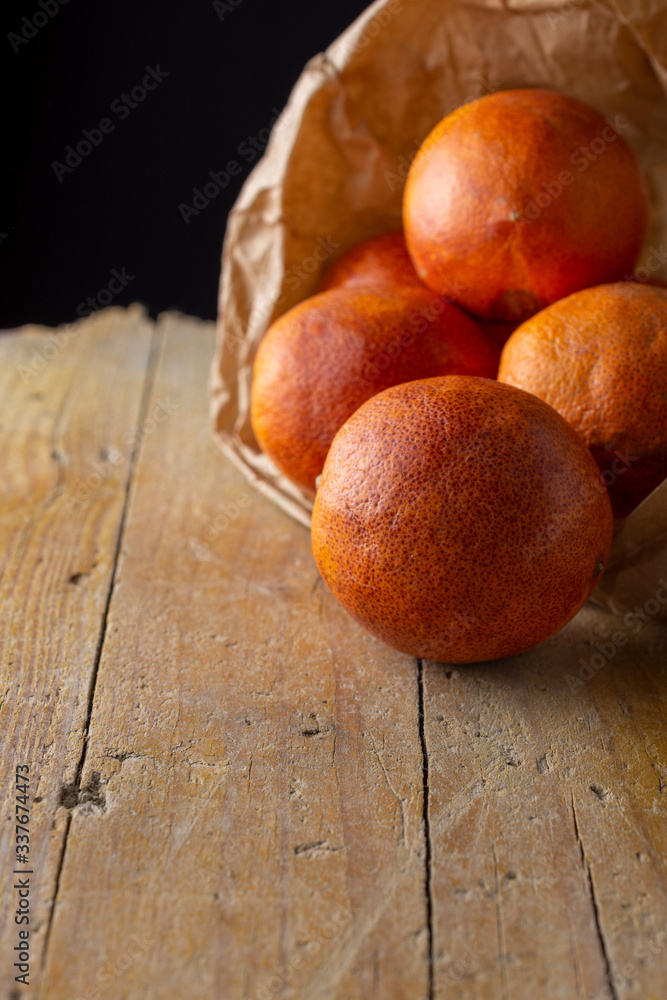 Close-up of blood oranges in paper bag, with selective focus, on rustic wooden board and black background, vertical, with copy space Close-up of blood oranges in paper bag, with selective focus, on rustic wooden board and black background, vertical, with copy space