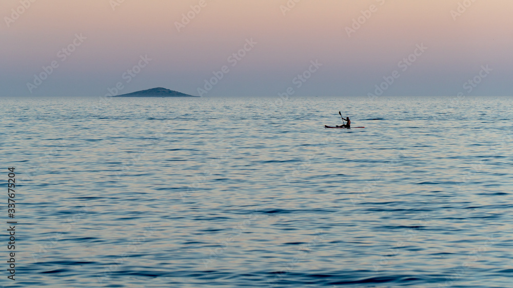 Canoeist sailing alone on the calm sea at dusk.