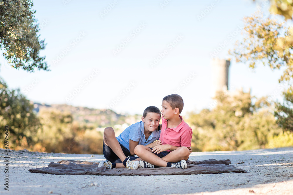 Two boys sitting on the floor in nature playing, hugging, laughing and being silly. Siblings connection. Two boys sitting on the floor in nature playing, hugging, laughing and being silly. Siblings connection.