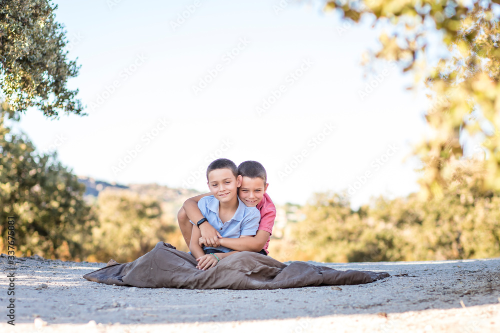 Two boys sitting on the floor in nature, hugging, playing, laughing, being silly and telling each other secrets. Siblings connection.