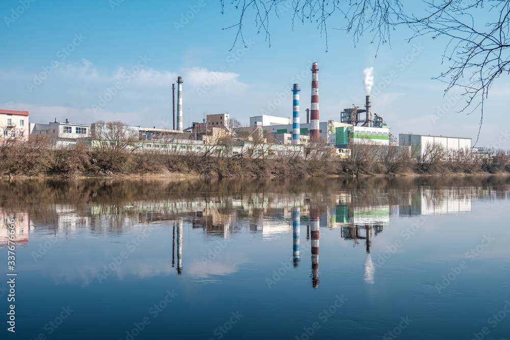 pipes of woodworking enterprise plant sawmill near river. Air pollution concept. Industrial landscape environmental pollution waste of thermal power plant pipes of woodworking enterprise plant sawmill near river. Air pollution concept. Industrial landscape environmental pollution waste of thermal power plant