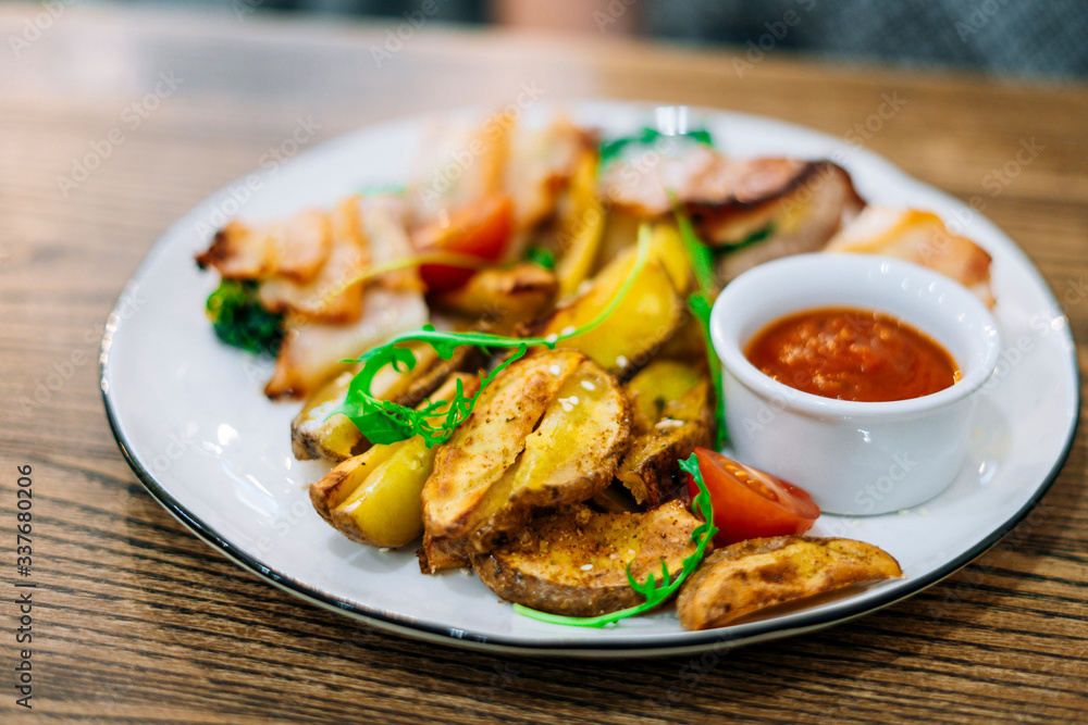 Chicken meat, roast potatoes and sauce on a round white plate. Potatoes with ketchup. Chicken meat, roast potatoes and sauce on a round white plate. Potatoes with ketchup.
