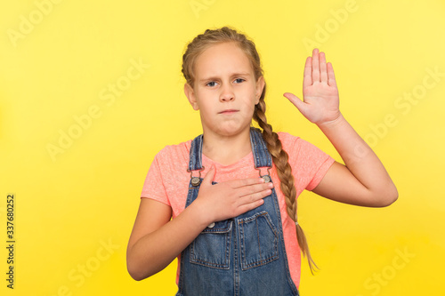 Canvas Print I promise to be honest! Portrait of serious responsible little girl with braid in denim overalls raising palm to take oath, child swearing to tell truth