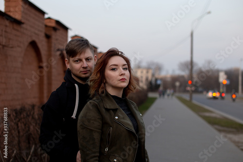 Young beautiful girl standing with his back to the guy. Young loving couple on background of brick wall. © Alena Sharuk