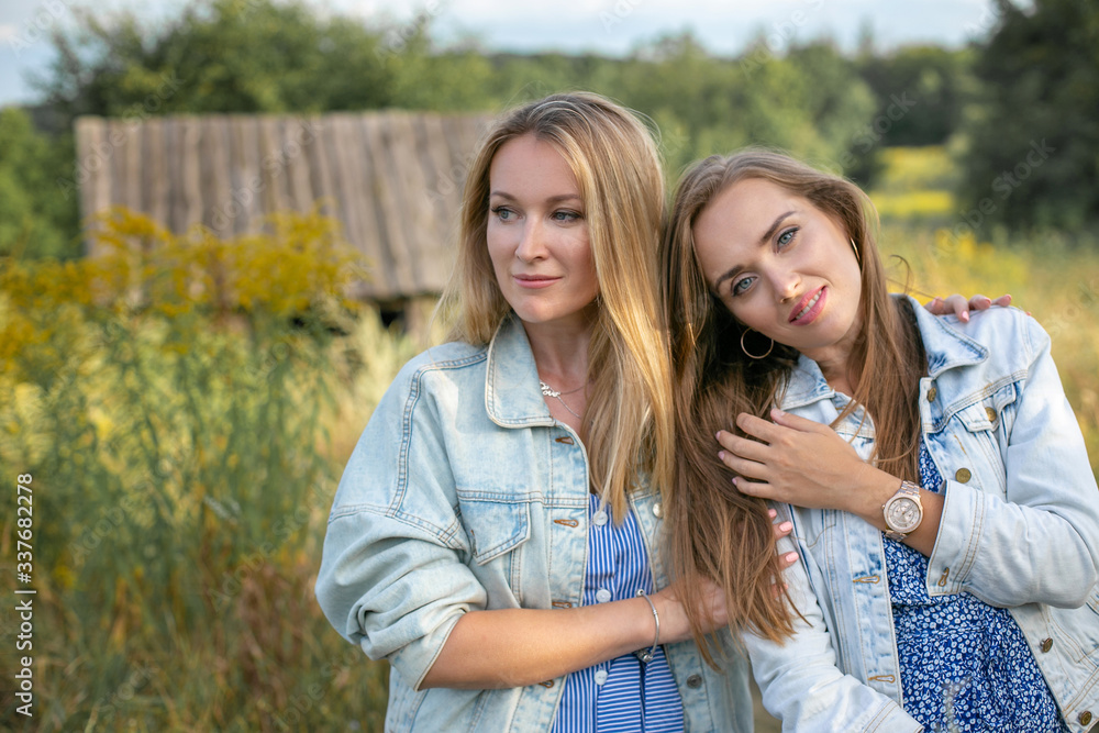 Fototapeta premium horizontal closeup portrait of two cute adult sisters against the backdrop of nature and rural landscape