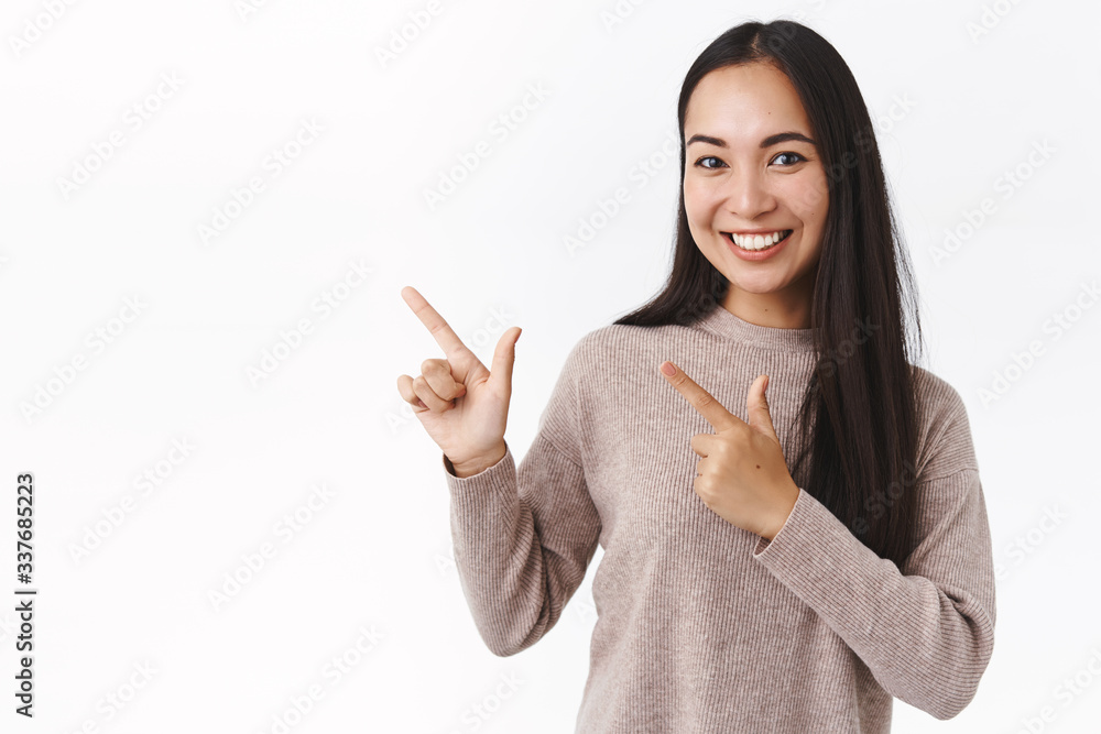 Cheerful, good-looking asian female with long dark hair, winter sweater, pointing upper left corner to promote corporate banner or advertisement, smiling pleased, recommend use code or try yourself Cheerful, good-looking asian female with long dark hair, winter sweater, pointing upper left corner to promote corporate banner or advertisement, smiling pleased, recommend use code or try yourself