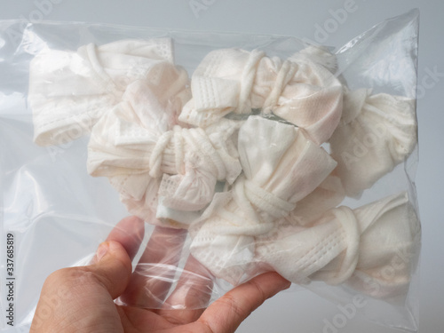 A hand is holding a plastic bag of used and folded surgical masks. The used masks is a tool to protect themselves from  COVID-19 epidemic so that the masks become an infectious waste. 