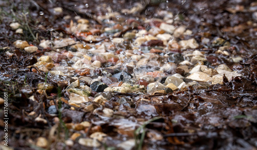 Trickles of water from the melting snow falling with splashes on the fine gravel. Spring streams. Off-season. Close up. Selective focus.