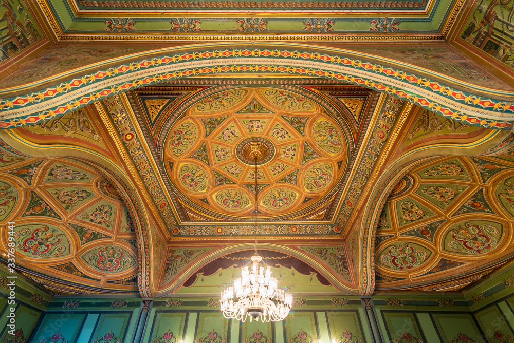 Ceiling at royal era historic Manasterly Palace decorated with colorful and golden floral paintings, and lighted chandelier, Cairo, Egypt