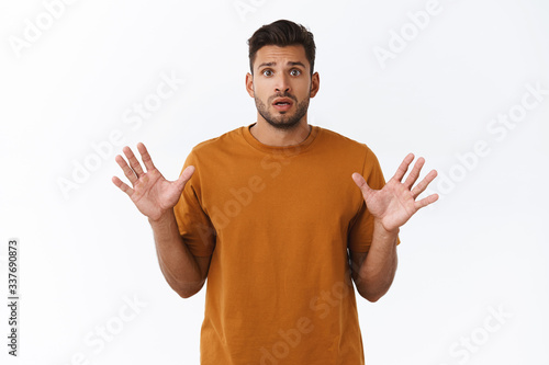 Worried cute bearded guy in t-shirt, raise hands up in stop gesture, shaking hands nervously, anxious as being late with buying present, frowning sad and indecisive standing white background upset photo