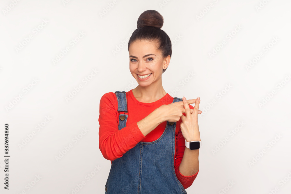 Portrait of optimistic happy stylish girl with hair bun in denim overalls showing hashtag gesture and smiling to camera, symbol of viral content, blog trends. indoor studio shot, white background Portrait of optimistic happy stylish girl with hair bun in denim overalls showing hashtag gesture and smiling to camera, symbol of viral content, blog trends. indoor studio shot, white background
