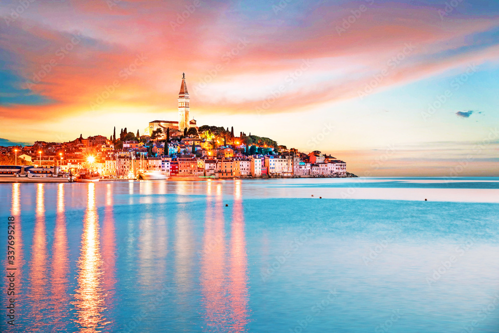 Beautiful magical city landscape with sea, colorful houses and an ancient tower in Rovinj, Croatia at evening lights at sunset. popular tourist attraction. (vacation, rest - concept)