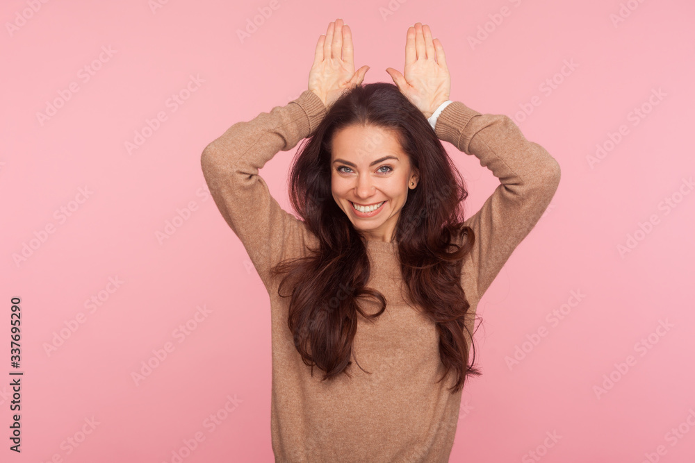 I am rabbit! Portrait of childish carefree young woman with brunette wavy hair showing bunny ears on head and smiling playfully, flirting having fun. indoor studio shot isolated on pink background I am rabbit! Portrait of childish carefree young woman with brunette wavy hair showing bunny ears on head and smiling playfully, flirting having fun. indoor studio shot isolated on pink background
