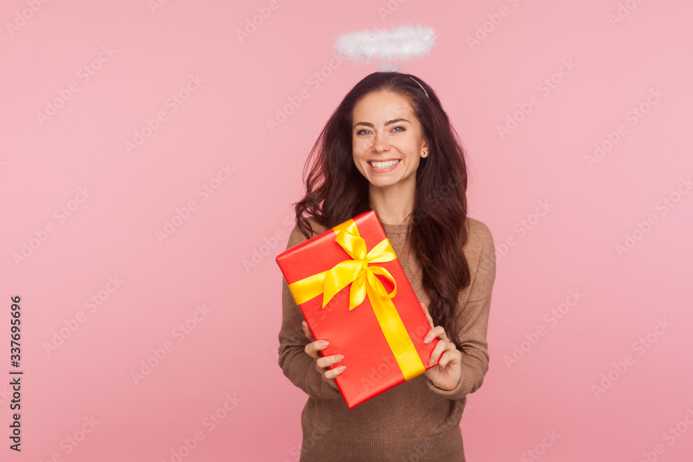 Portrait of happy beautiful angelic young woman with halo holding big present and smiling to camera, satisfied with gift, celebrating birthday, anniversary. studio shot isolated on pink background Portrait of happy beautiful angelic young woman with halo holding big present and smiling to camera, satisfied with gift, celebrating birthday, anniversary. studio shot isolated on pink background