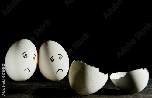 two sad eggs look at a broken egg on a black background