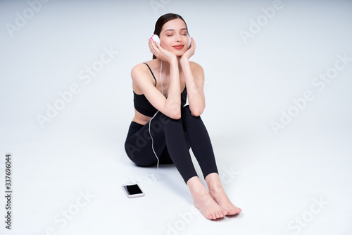 Cute young girl in a sporty black uniform listens to music and rests after a workout.