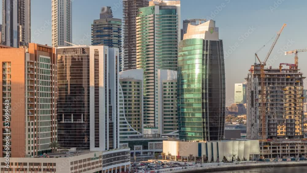 Futuristic skyscrapers near canal aerial timelapse with blue sky and restaurants in coast at sunny day on Business Bay with reflection from glass, Dubai, United Arab Emirates Futuristic skyscrapers near canal aerial timelapse with blue sky and restaurants in coast at sunny day on Business Bay with reflection from glass, Dubai, United Arab Emirates