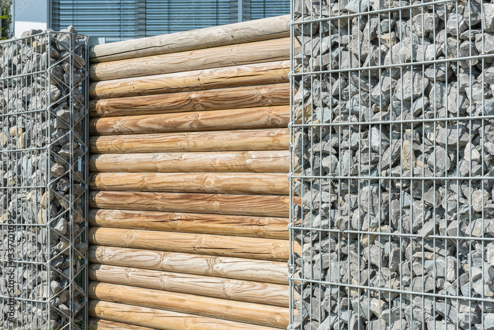 Mauer aus Gabionen und Holzstämmen im Garten StockFoto Adobe Stock