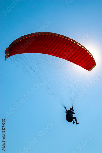 The sun is shining through the red paraglide of an unrecognizable paraglider (silhouette). (ID: 337702012)