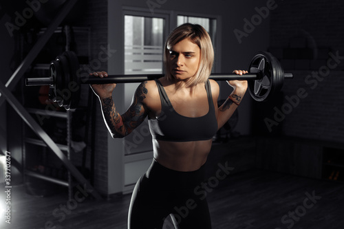 Athletic young blonde woman doing heavy barbell exercise in fitness class.
