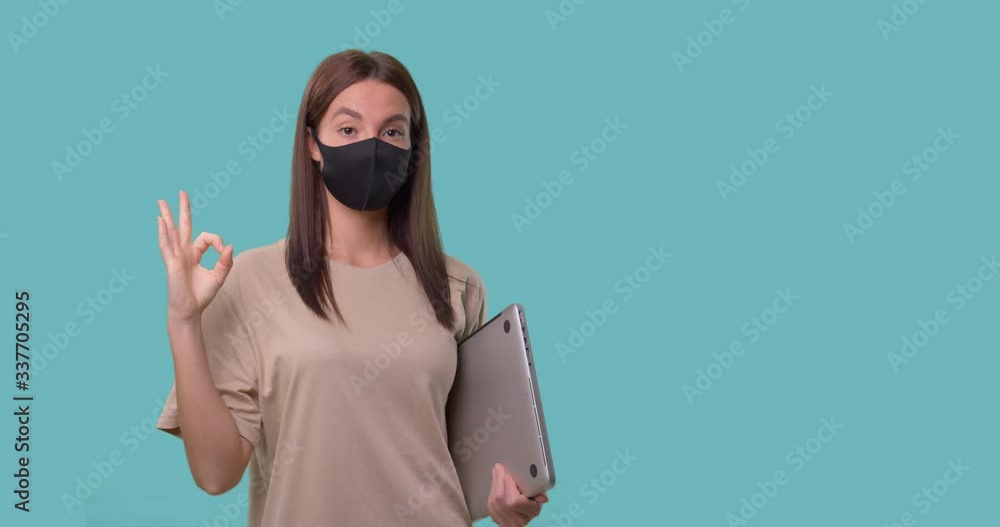 woman in mask shows ok sign, she holds her laptop computer, freelance concept woman in mask shows ok sign, she holds her laptop computer, freelance concept