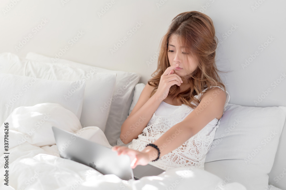 Young beautiful Asian female using laptop or notebook for working at home or shopping online while laying on bed in her bedroom. Communication Technology, marketing online, social media concept. Young beautiful Asian female using laptop or notebook for working at home or shopping online while laying on bed in her bedroom. Communication Technology, marketing online, social media concept.