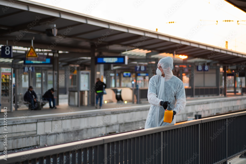 Fototapeta premium Ein Mann in einem Schutzanzug desinfiziert an einem Bahnhof ein Geländer, Kampf gegen die Ausbreitung des Coronavirus 