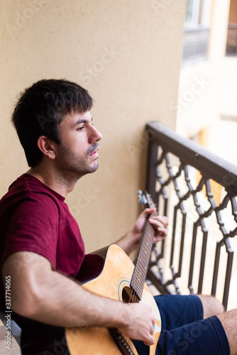 Man playing guitar on the balcony while spending time at home
