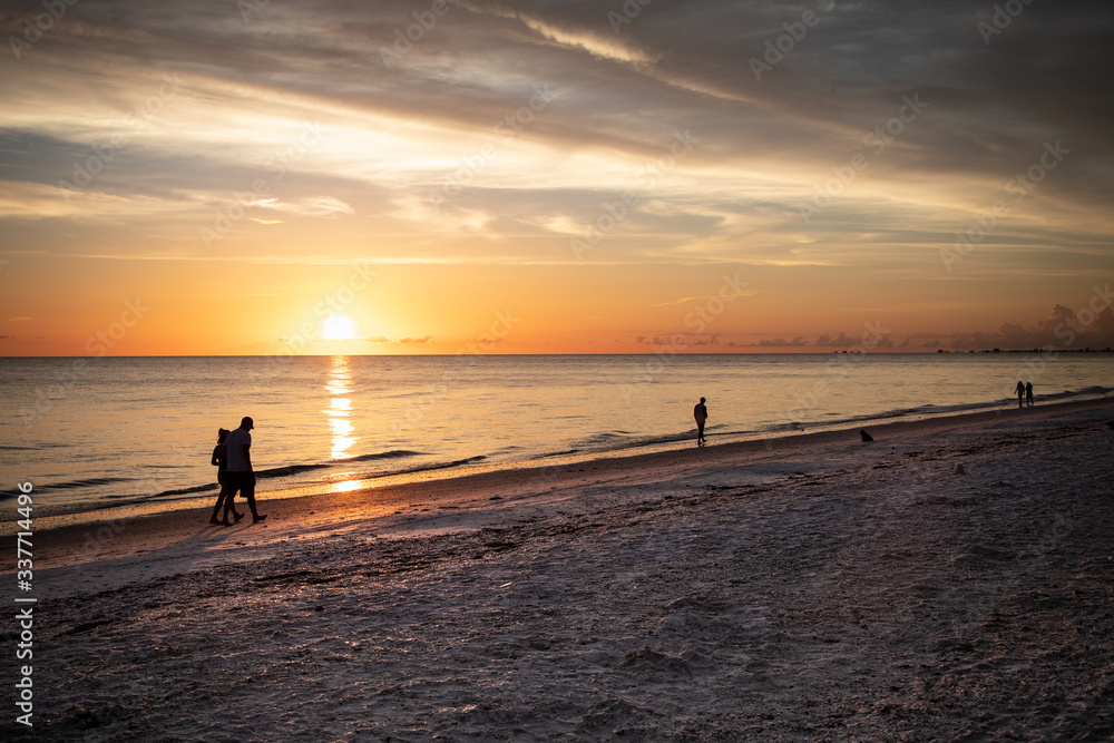 Several people and a dog enjoy a walk at sunset in Bonita Beach, FL