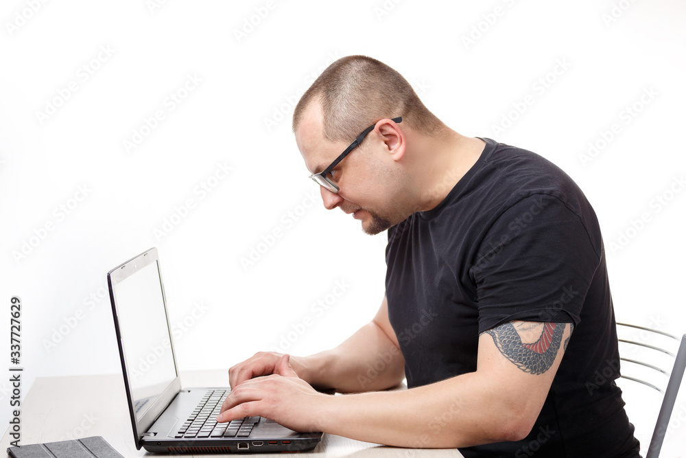 A man sits at a table with glasses and works on a laptop. On a white background. A man sits at a table with glasses and works on a laptop. On a white background.