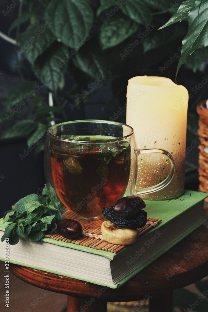 Dark mystic and calm mood. Book and hot tea with mint and honey on table with green plant