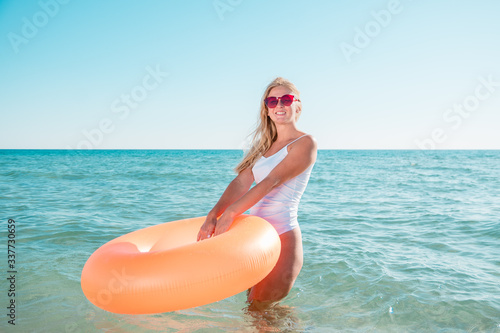 Girl with inflatable rubber enters the sea. Model goes into clear blue water on a hot day and holding orange ring.