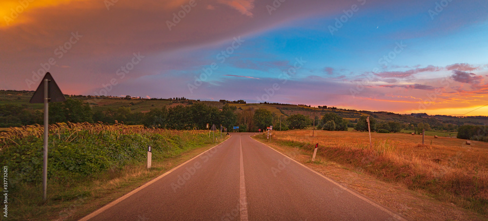 Breathtaking wide angle view of the beautiful sunset over the road with the storm front and orange clouds in Tuscany, Italy