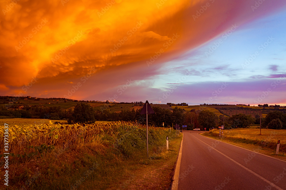 Astonishing wide angle view of the sunset over the road with the storm front and orange clouds in Tuscany, Italy