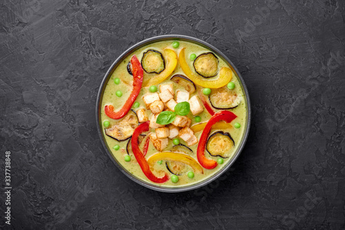 Vegetarian Thai Green Curry with tofu in black bowl at dark slate background. Veg Green Thai Curry is thailand cuisine dish with green chillies paste, basil, spices and vegetables. Copy space