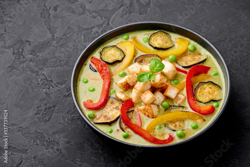 Vegetarian Thai Green Curry with tofu in black bowl at dark slate background. Veg Green Thai Curry is thailand cuisine dish with green chillies paste, basil, spices and vegetables. Thai Food