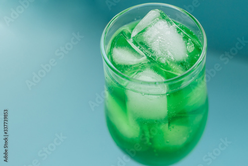 A glass of green cocktail with ice on a blue background.Tableware for alcohol.A glass for champagne and wine.Chilled drinks.