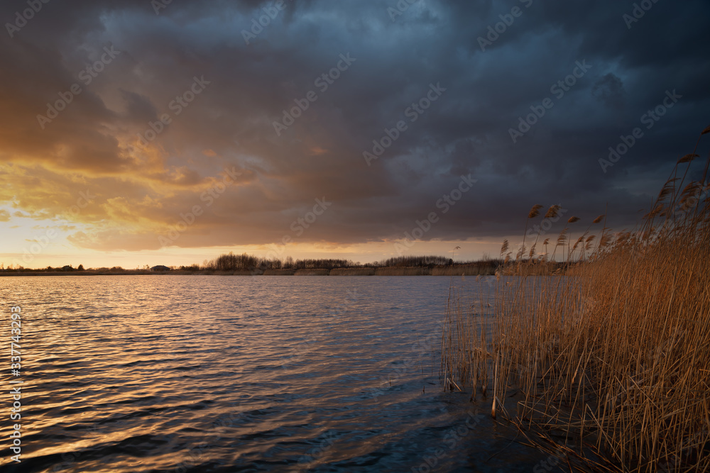 Dark clouds lit by the sun on a lake with reeds