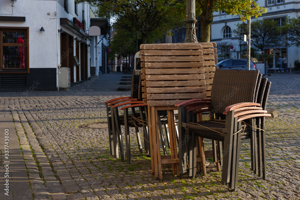 Selected focus at stack of outdoor chairs of pub, cafe and restaurant shutdown during quarantine from contagion of COVID-19 on walking street in old town.