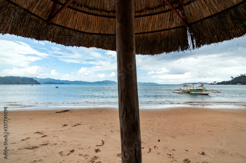 Fototapeta Naklejka Na Ścianę i Meble -  Seascape shot in a cloudy day from under a straw umbrella in the beach of Port Barton, Palawan, Philippines