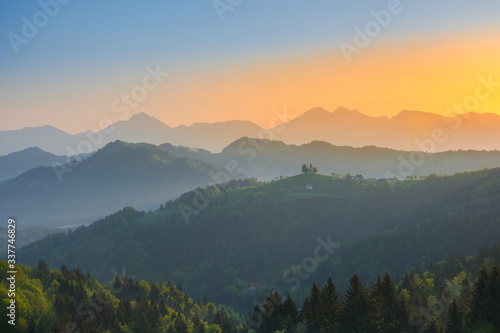 Slovenian breathtaking landscape at sunrise with Julian Alps and charming little church of Sveti Tomaz (Saint Thomas) on a hill, in spring. Beautiful misty morning in the mountains, in Slovenia.
