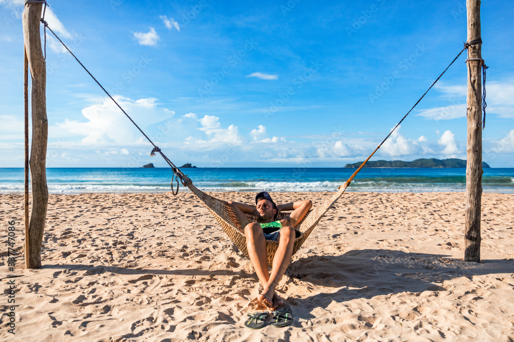A young tourist man lies on a hammock in Nacpan beach, near El Nido, Palawan, Philippines