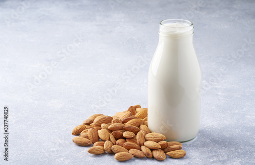 almonds and a bottle of almond milk on a light grey background. Vegan milk.