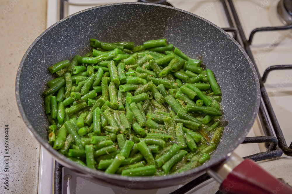 Fresh juicy green french beans are fried in a frying pan on a kitchen gas stove Fresh juicy green french beans are fried in a frying pan on a kitchen gas stove
