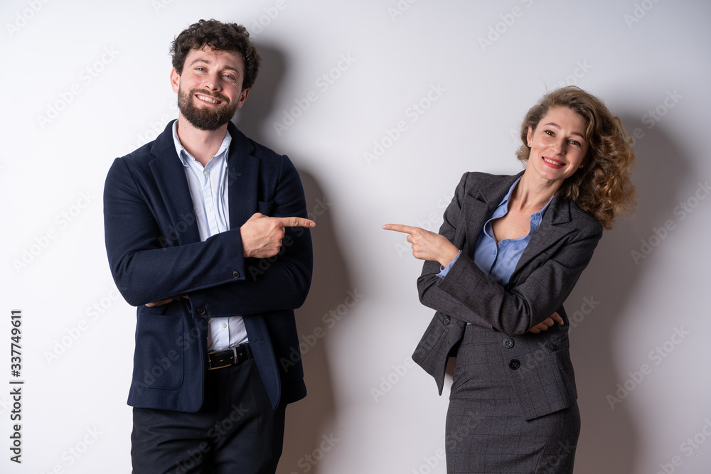 Man and woman in business attire pointing the finger at each other, looking at the camera, smiling Man and woman in business attire pointing the finger at each other, looking at the camera, smiling