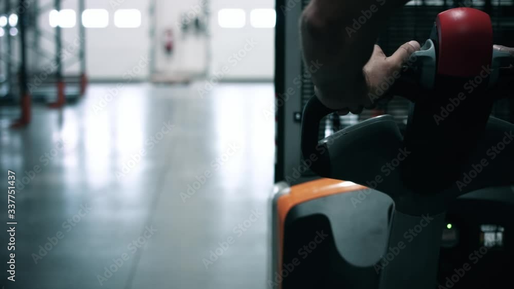 Close up of an operator who is on an electric pallet truck in a warehouse. We can see the hands of the operator who walks. Company and warehouse logistics Close up of an operator who is on an electric pallet truck in a warehouse. We can see the hands of the operator who walks. Company and warehouse logistics