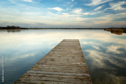 Wooden jetty towards the lake, horizontal reflection of clouds in water, Staw, Poland