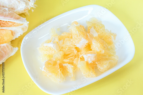 pomelo slices in a white plate close-up. background with peeled pomelo slices on the table.
