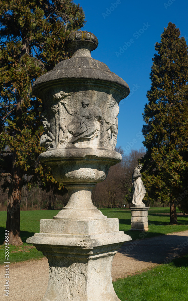 A stone sculpture in the public park of Vicenza: Parco Querini. On the surface scenes of Greek mythology are reproduced. Soft stone with traces of fossil shells. In the background a feminine statue.