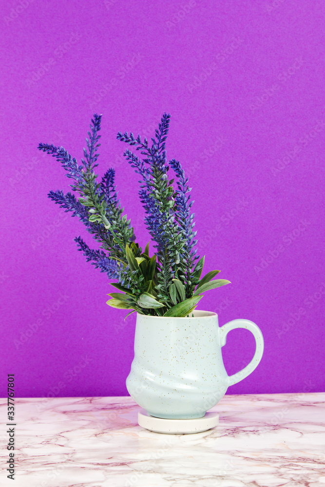 Lavender flowers in a pastel blue mug on a marble table and purple background Lavender flowers in a pastel blue mug on a marble table and purple background
